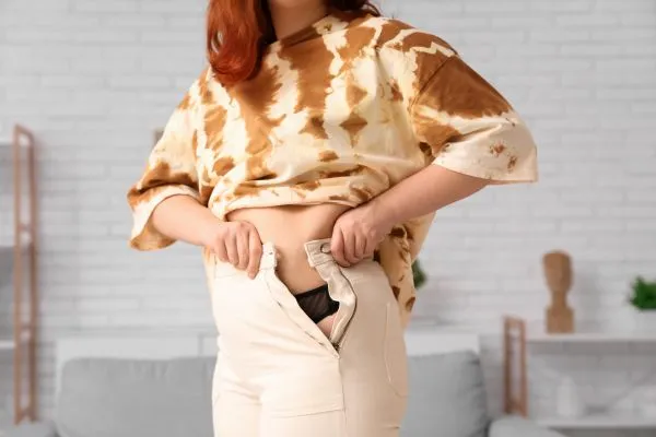 Image of woman trying to do her trousers up after pregnancy weight gain Marlow